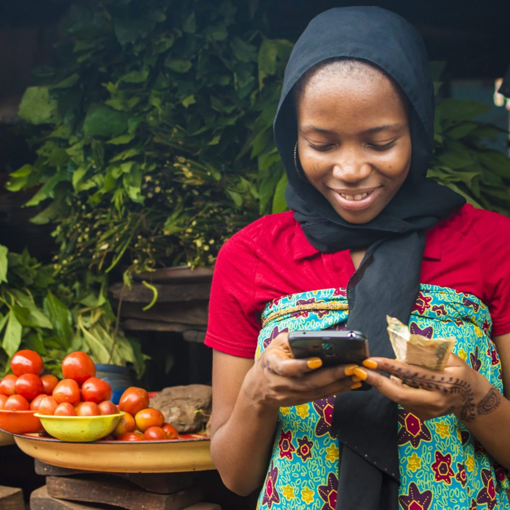 young african woman selling in a local market smiling while using her mobile phone