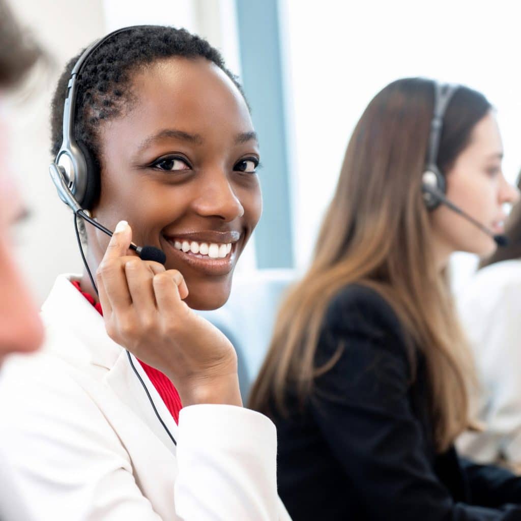 Smiling beautiful African American woman working in call center office with diverse team as the customer care operators